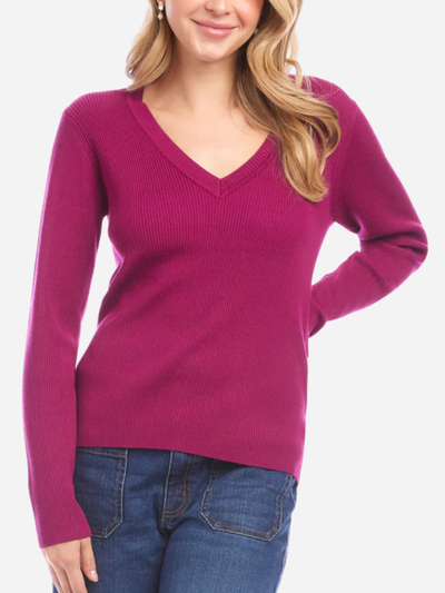 Woman wearing a magenta v-neck sweater and blue jeans on a white background
