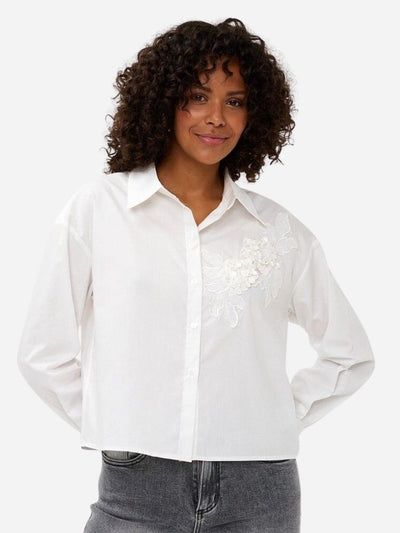 Woman wearing a white blouse with floral embroidery on a plain background