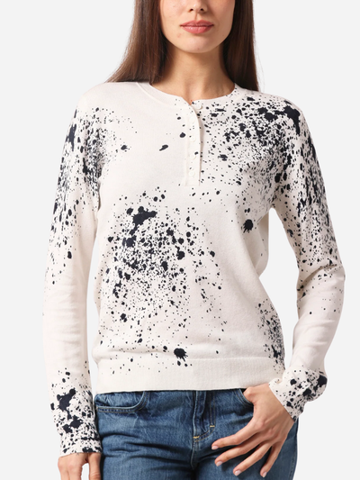 Woman wearing a white sweater with black splatter pattern on a plain background