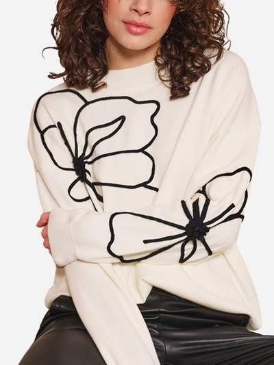 White sweater with black floral designs worn by a woman on a white background