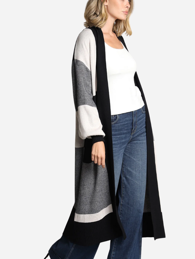 Woman wearing a long, black and gray cardigan over a white top and blue jeans on a white background