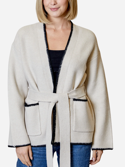 Woman wearing a cream-colored cardigan with black trim on a white background