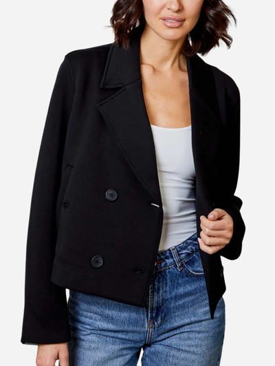 Person wearing a black blazer over a white top and blue jeans on a plain background