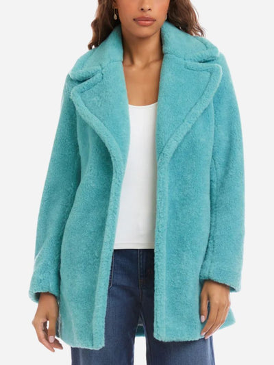 Person wearing a teal faux fur coat with a white top and blue jeans on a white background