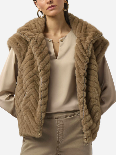 Woman wearing a brown fur vest over a beige outfit on a white background