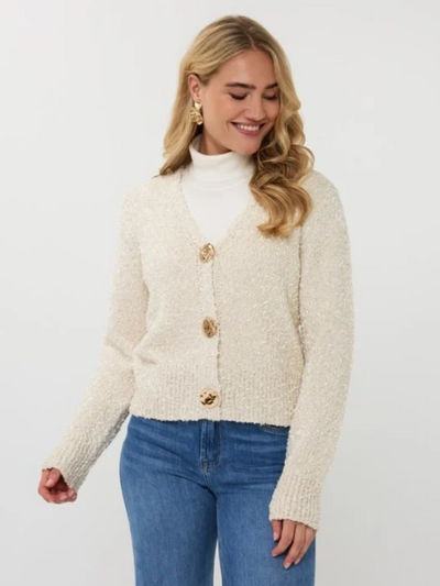 Woman wearing a cream cardigan with gold buttons on a white background